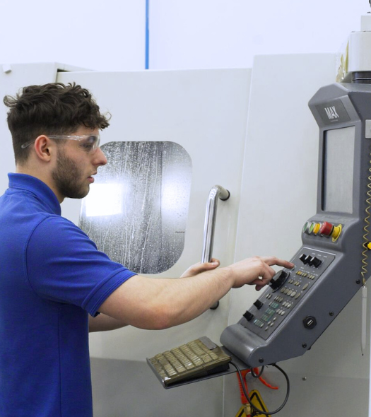 Man wearing a blue polo shirt and safety goggles operating a CAD machine