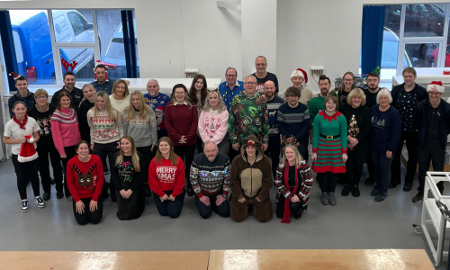 Christmas group photo taken in an office with people wearing festive jumpers and hats
