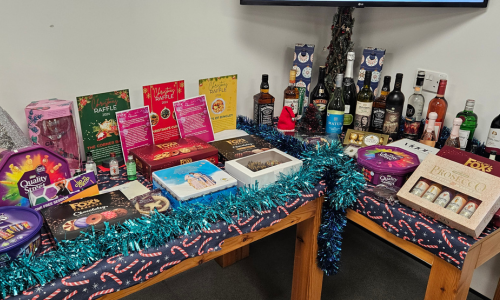 Corner table loaded with Christmas raffle prizes including boxes of biscuits and chocolates and bottles of alcohol