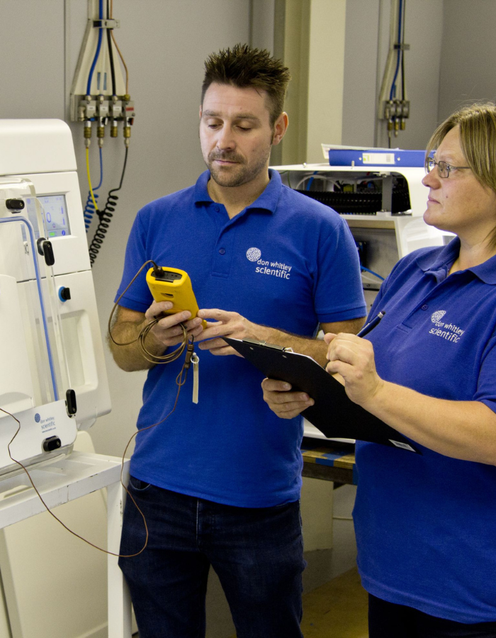 2 DWS employees operating a machine and taking notes on a clipboard.